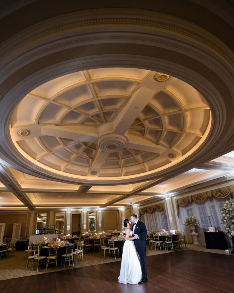 Bride and groom sharing a quiet moment on the dance floor beneath the ornate ceiling of The Muttontown Club ballroom.