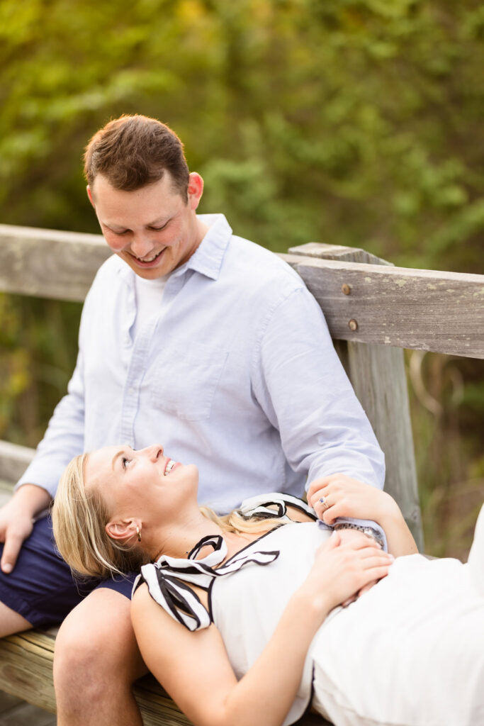 Emily reclines beside Corbin on the wooden boardwalk during their relaxed Long Island engagement session.
