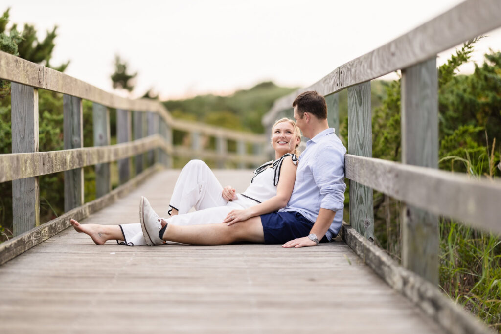 Emily and Corbin sit together on the boardwalk surrounded by coastal greenery at Robert Moses.