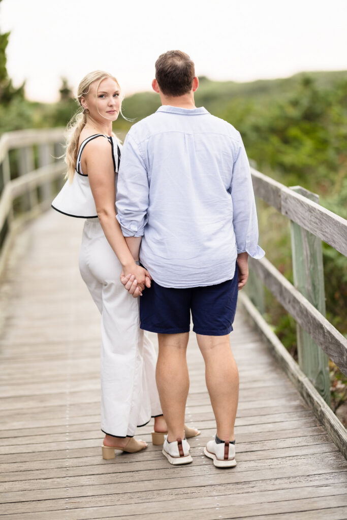 Emily looks back toward the camera while holding Corbin's hand during their windy Robert Moses engagement session.