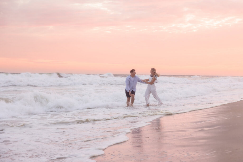 Emily and Corbin laugh together in the surf during their sunset beach engagement session on Long Island.