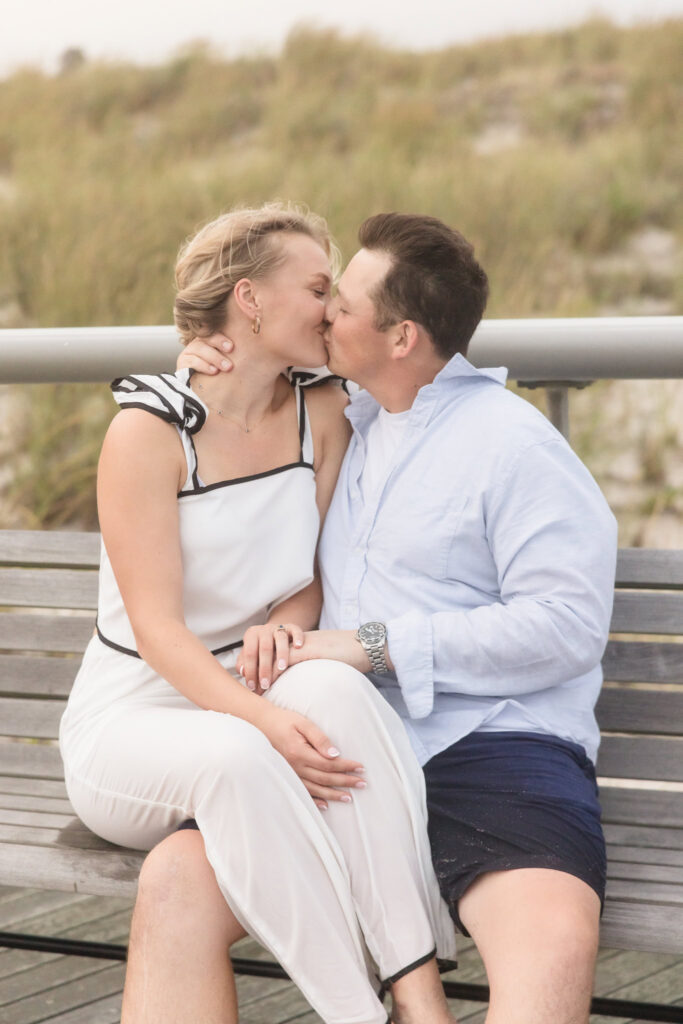 Emily and Corbin kiss while sitting together on a bench during their Robert Moses engagement session.