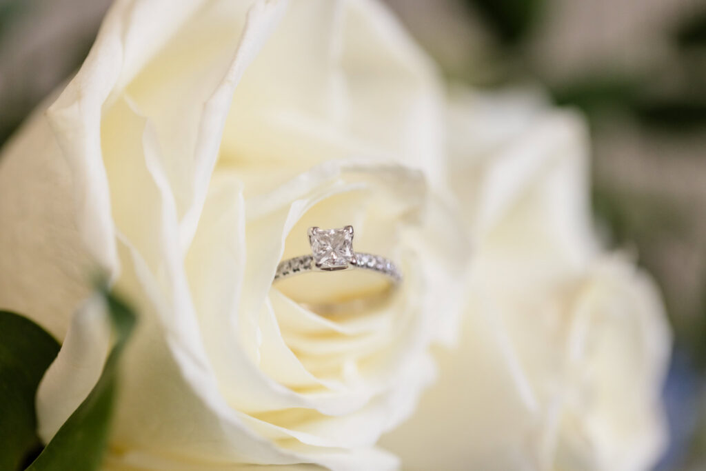Diamond engagement ring nestled inside the petals of a white rose before a Sea Cliff Manor wedding.