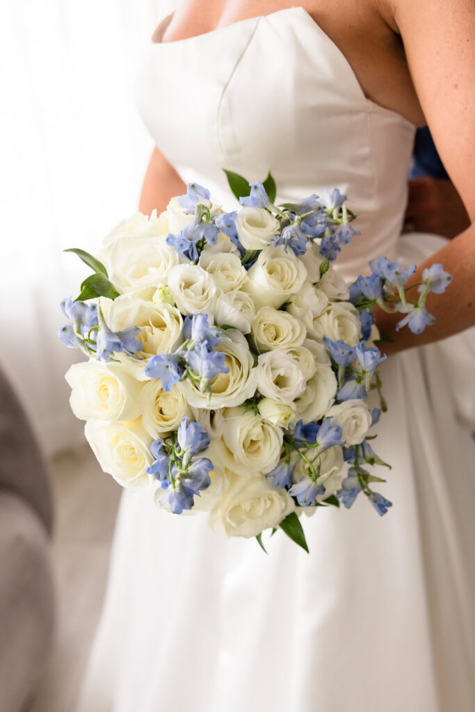 Bride holding a romantic wedding bouquet of white roses and soft blue flowers before her Sea Cliff Manor ceremony.