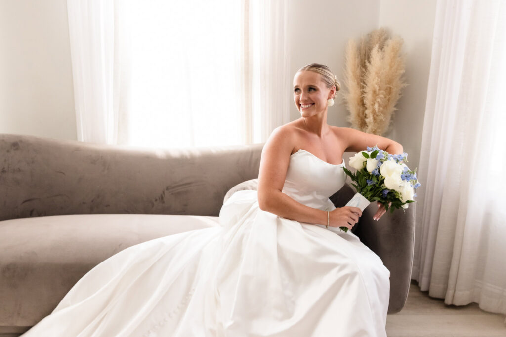 Smiling bride seated with her white and blue bouquet before her Sea Cliff Manor wedding.