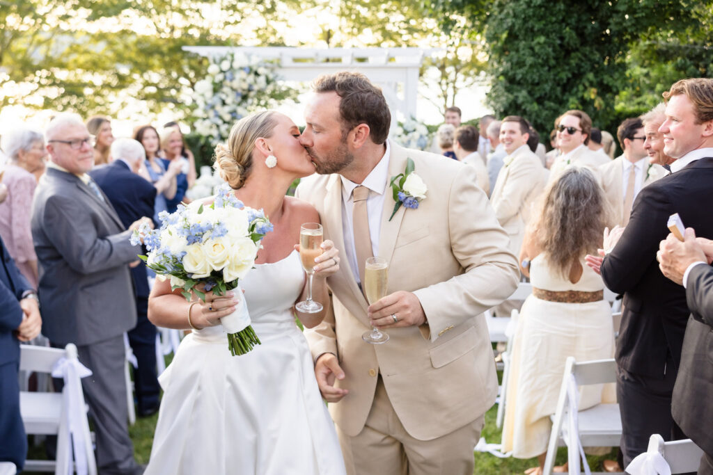 Newlyweds Quinn and Josh kiss with champagne after their Sea Cliff Manor ceremony, surrounded by guests from their large bridal party wedding.
