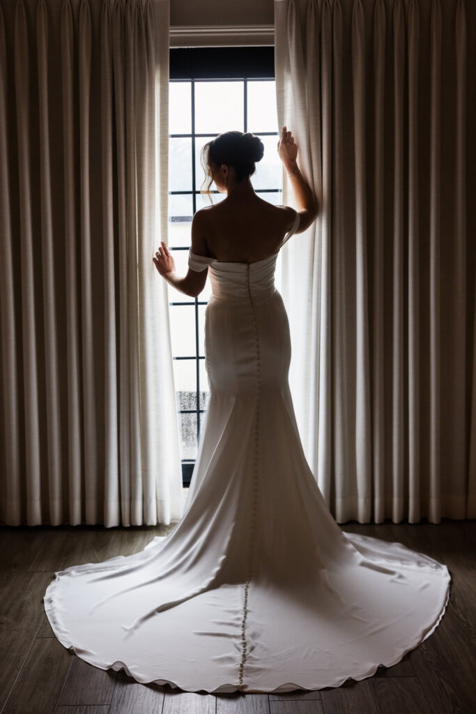 Bride standing beside a window in her wedding gown during preparations at The Swan Club in Roslyn.
