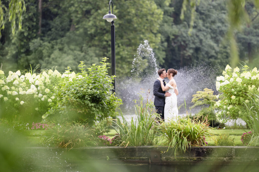 Bride and groom kiss in the gardens with a fountain behind them at The Swan Club in Roslyn.