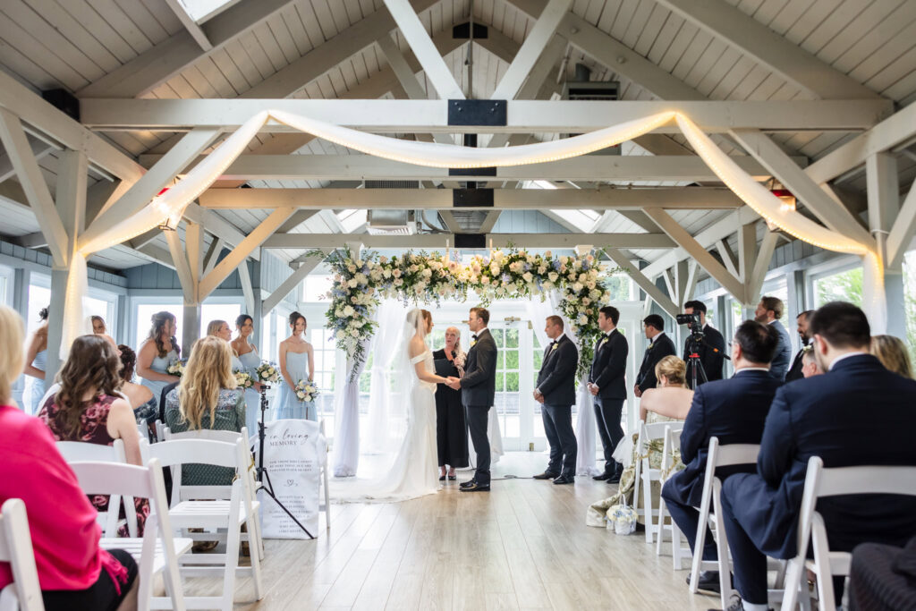 Bride and groom exchanging vows beneath a floral arch in the ceremony pavilion at The Swan Club in Roslyn
