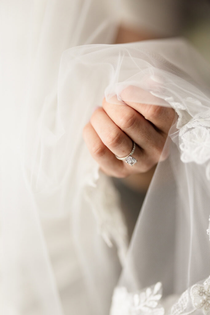 Close-up of the bride’s diamond engagement ring as she holds the delicate fabric of her veil.