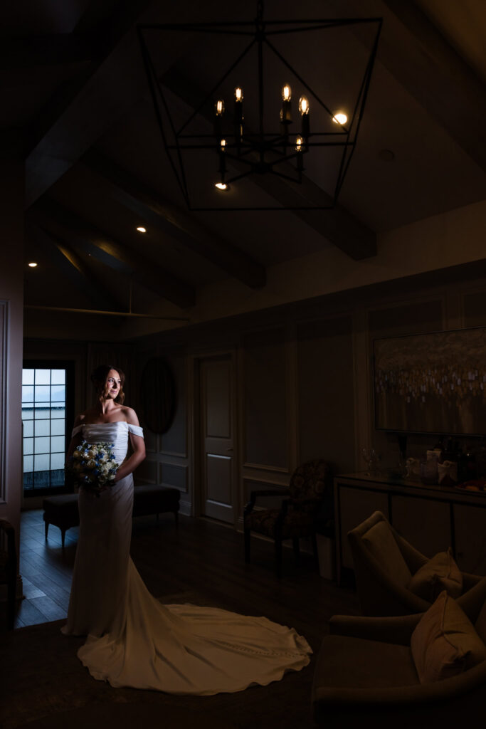 Dramatic bridal portrait in a softly lit room with the bride holding her blue-and-white bouquet.