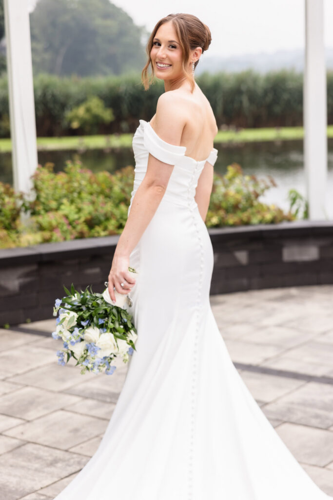 Bride looking back and smiling while holding her bouquet beside the water at Swan Club on the Harbor.