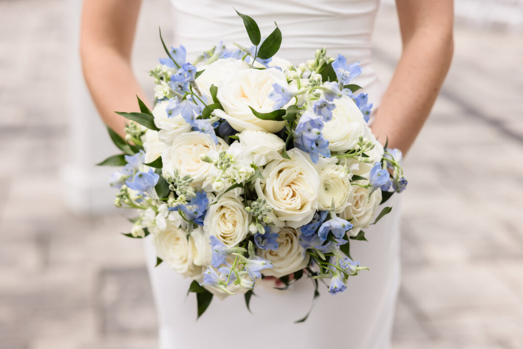 Close-up of a bridal bouquet featuring white roses and soft blue flowers with fresh greenery.