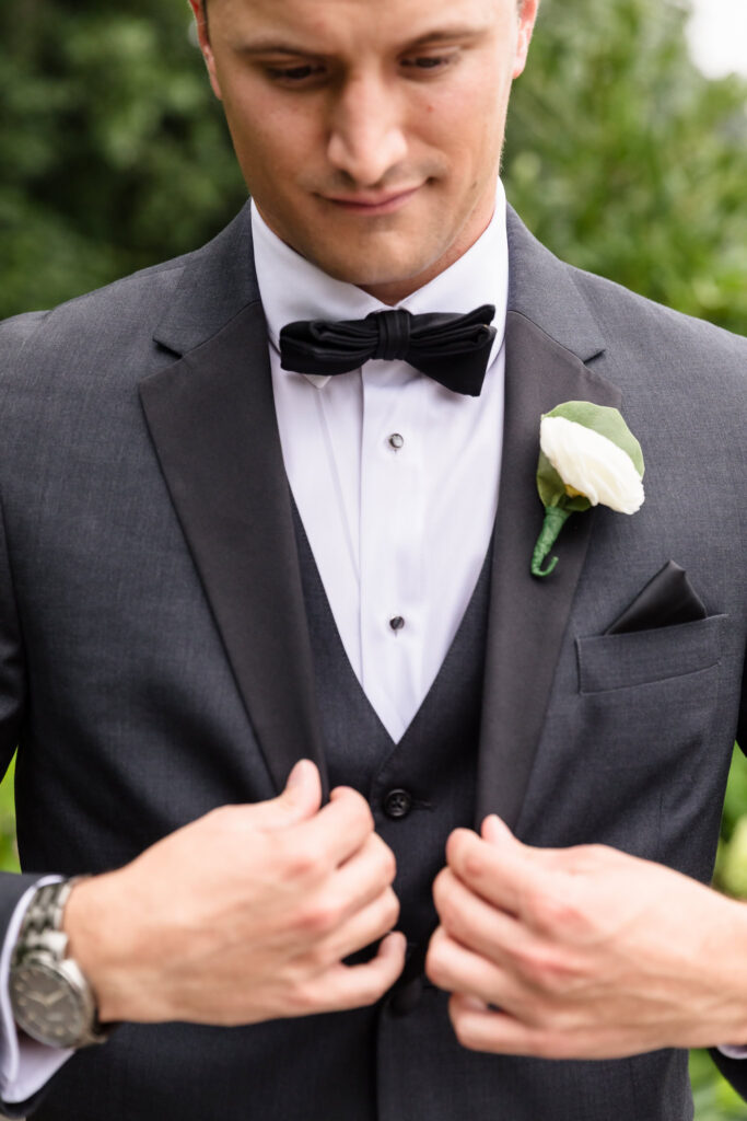 Close-up of the groom’s charcoal tuxedo, black bow tie, white boutonniere, and watch.