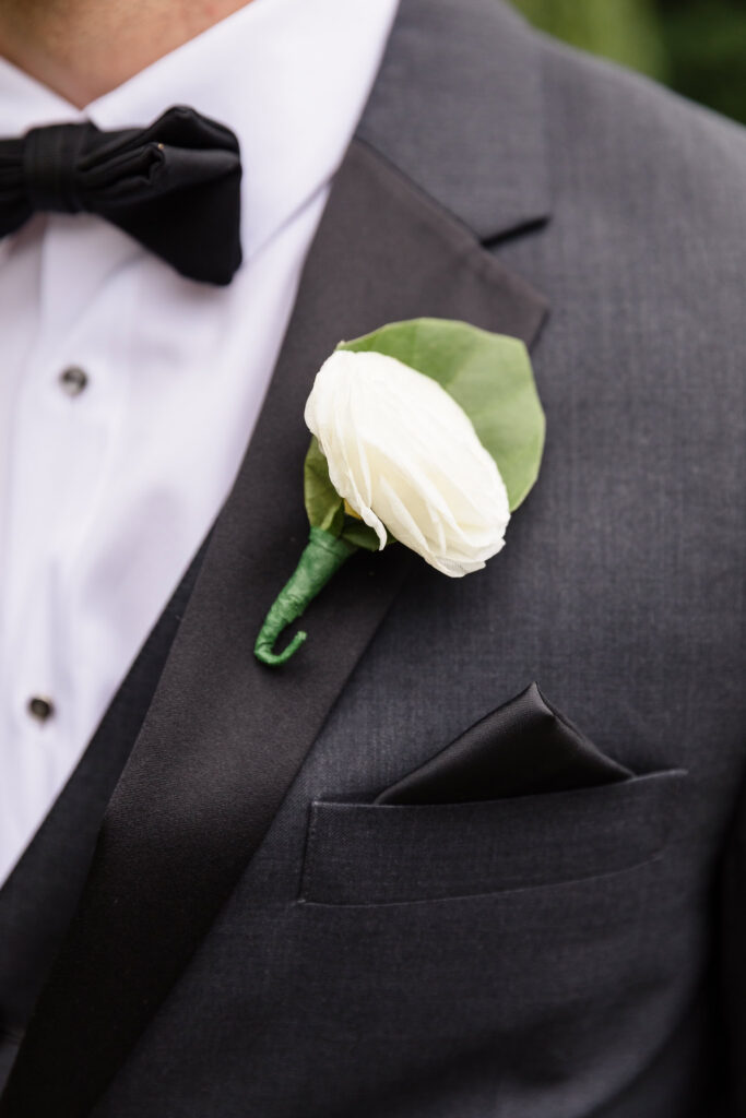 Close-up of Mark’s white rose boutonniere against his dark tuxedo at his Swan Club wedding.