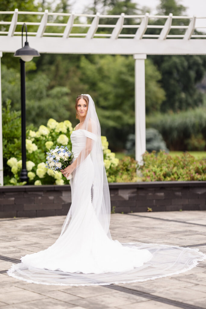 Tori holding her blue and white bouquet during a bridal portrait beneath the white pergola at The Swan Club.