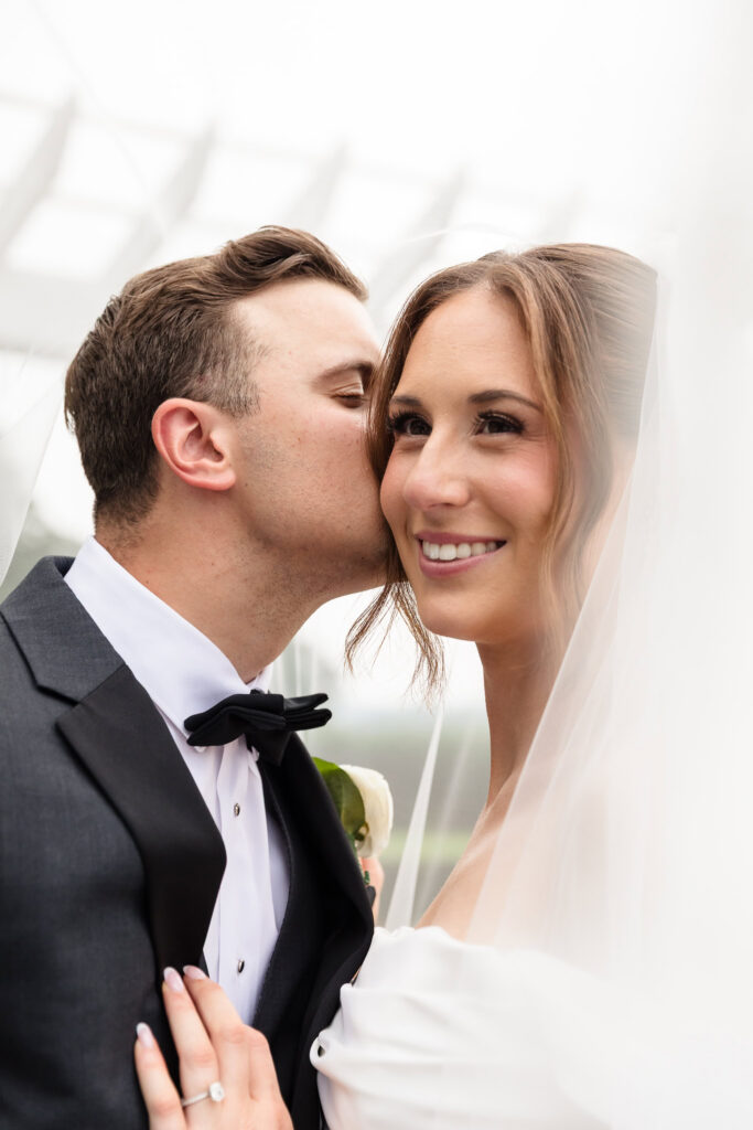 Mark kisses Tori beneath her veil during their Swan Club wedding portraits.