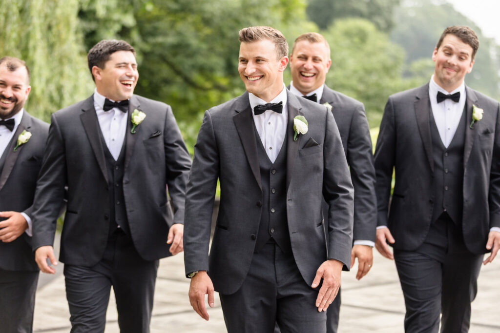 Mark laughs with his groomsmen in black tuxedos during wedding party portraits at The Swan Club.