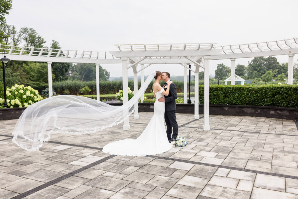 Tori and Mark kiss beneath the pergola as her long veil blows through the air at The Swan Club.