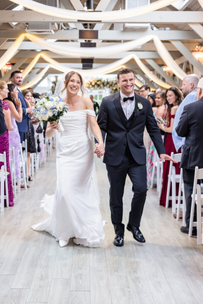 Newlyweds Tori and Mark smile and hold hands as they walk down the aisle after their Swan Club ceremony.
