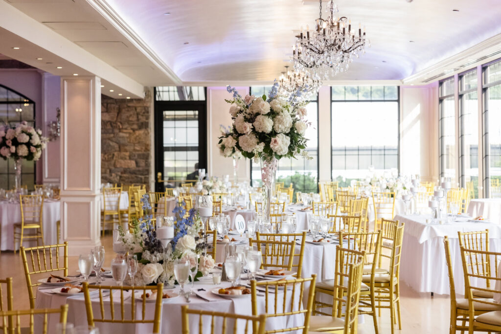 Swan Club wedding reception room with tall white floral centerpieces, gold chairs, chandeliers, and blue floral accents.