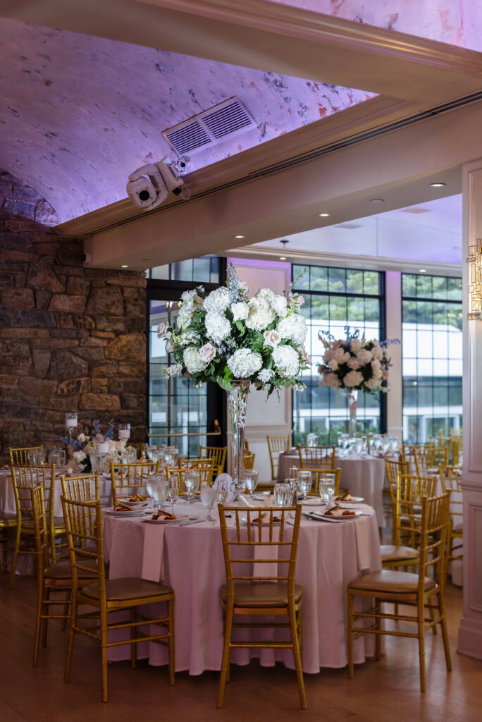 Tall white hydrangea and rose centerpiece surrounded by gold chairs at Tori and Mark’s Swan Club reception.