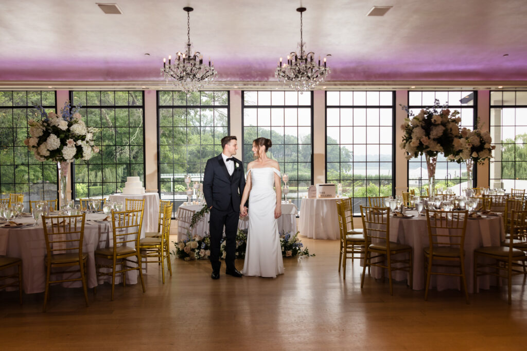 Tori and Mark stand together beneath crystal chandeliers inside their Swan Club wedding reception.