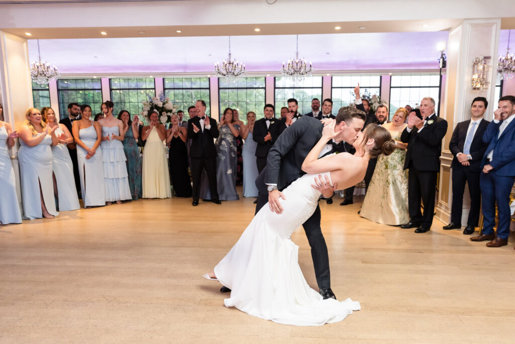 Tori and Mark kiss during a first dance dip as family and friends cheer at their Swan Club wedding reception.