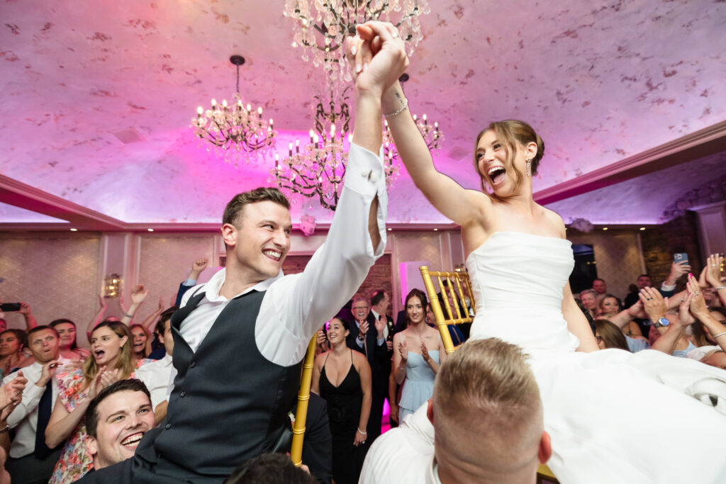 Tori and Mark celebrate together while lifted on chairs during their lively Swan Club wedding reception.