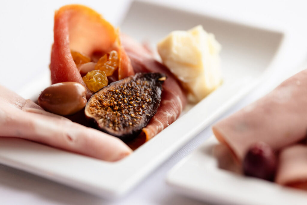 Close-up of a wedding appetizer plate featuring cured meats, fig, olives, raisins, and cheese.