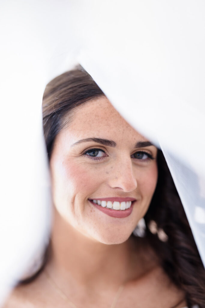 Close-up bridal portrait of Morgan smiling beneath her sheer white wedding veil.