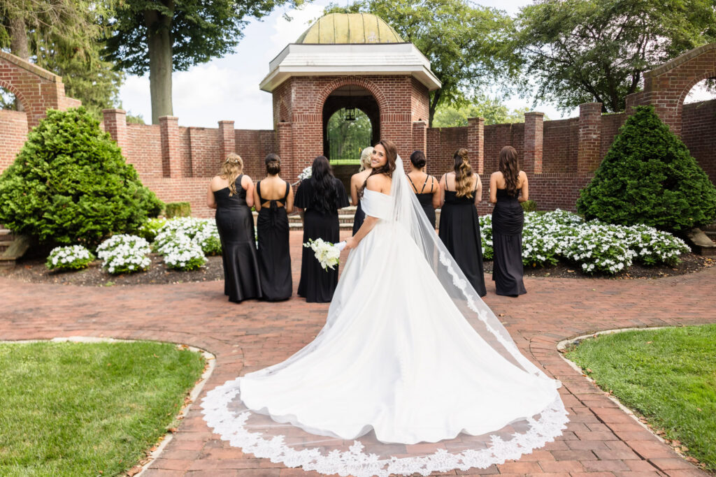 Morgan looking back toward the camera while her bridesmaids stand in black dresses in the garden courtyard.