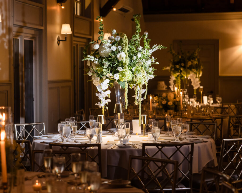 Tall white and green floral centerpiece surrounded by candlelit reception tables at the Old Field Club.