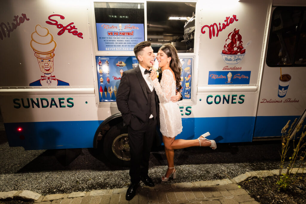 Bride and groom sharing an ice cream cone in front of a Mister Softee truck during their wedding celebration.